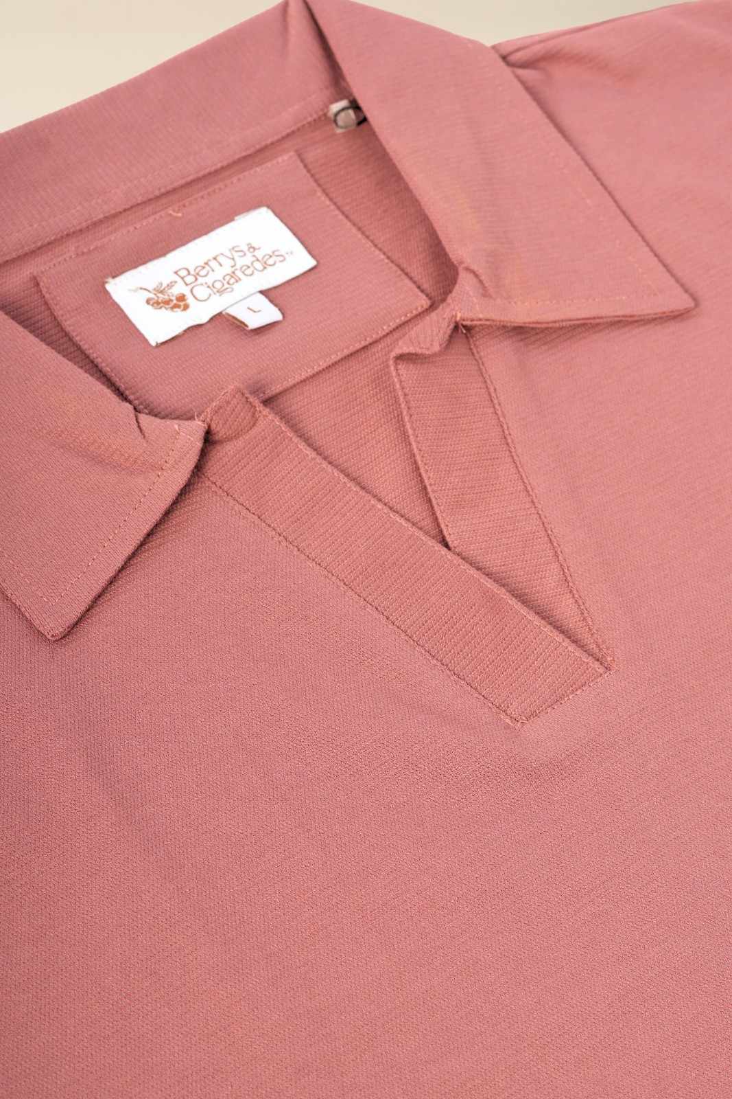 Close-up of Berrys & Cigaredes brand label on dusty rose women's polo shirt, displaying premium woven tag on quality textured fabric
