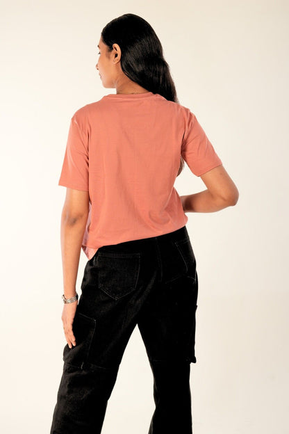 Back view of coral pink women's t-shirt with relaxed fit, paired with black cargo jeans - minimal casual wear