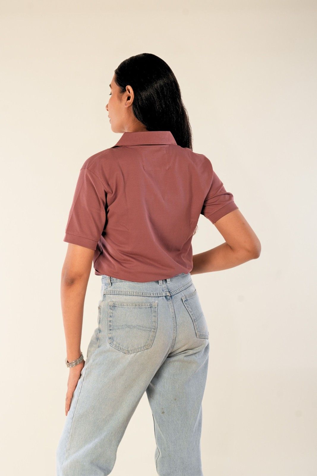 Woman wearing dusty rose slim-fit polo shirt from behind, light blue denim jeans, minimal urban style
