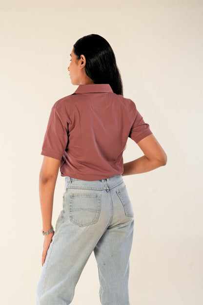Woman wearing dusty rose slim-fit polo shirt from behind, light blue denim jeans, minimal urban style