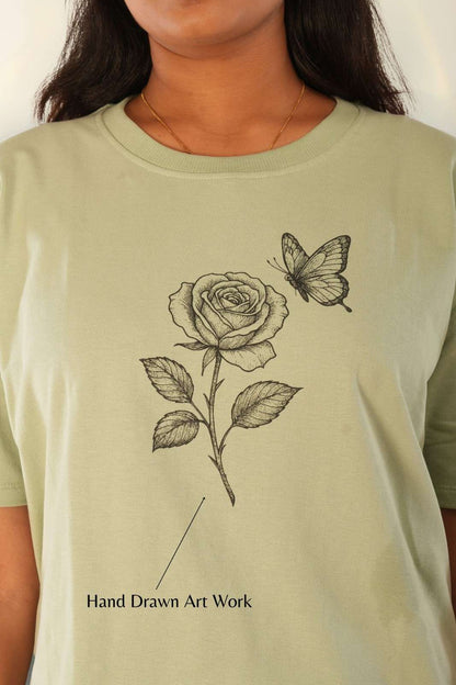  Hand-drawn rose and butterfly botanical line art on sage green oversized tee, close-up detail of premium knit fabric, women's minimal streetwear India