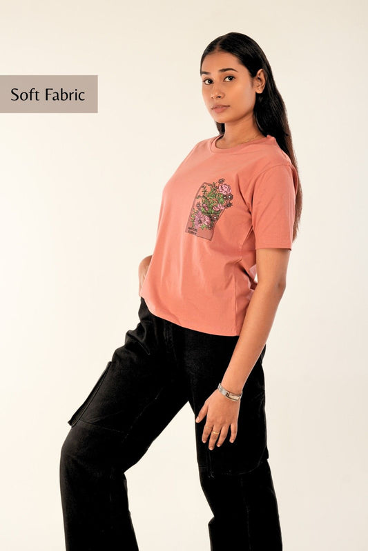 Coral pink women's t-shirt with floral garden artwork in raised puff and flat print, paired with black cargo jeans - casual streetwear